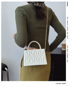 Close-up of white quilted box bag featuring gold chain and braided handle details