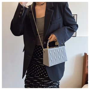 Close-up of light gray box bag featuring V-shaped pleated texture and gold chain strap