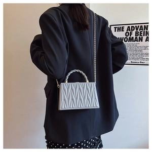 Detail of light grey V-quilted leather box bag with gold chain and woven handle