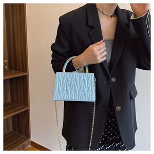 Detail of light blue matelassé handbag with twisted handle and golden chain strap