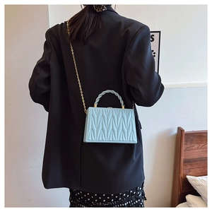 Detail of light blue pleated box bag featuring V-quilted texture and gold chain strap