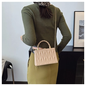 Detail of beige geometric quilted box bag with woven handle and gold chain strap