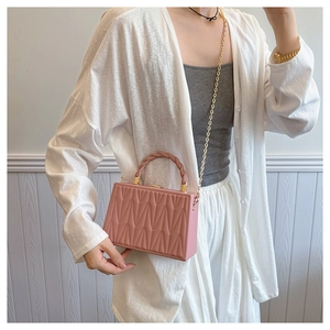 Detail of mauve box handbag featuring quilted wavy texture and woven handle design