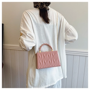 Detail of pink matelassé crossbody bag with twisted leather handle and gold chain strap
