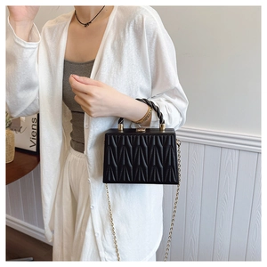 Detail of black geometric embossed box bag with gold chain strap on model in white outfit