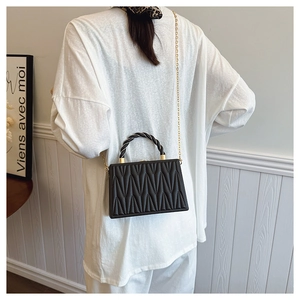 Detail of a black quilted crossbody bag with gold chain strap on a white shirt