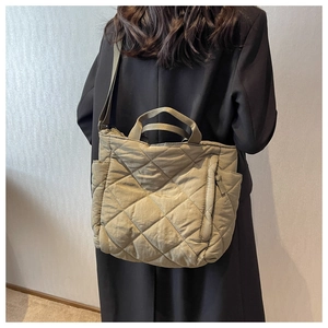 Detail of olive green quilted puffer tote bag with long strap shown in casual style