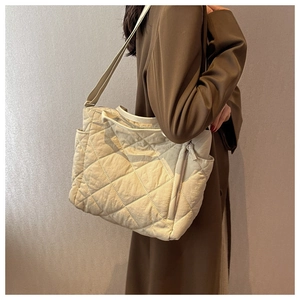 Detail of cream quilted tote bag with large capacity on model wearing brown coat