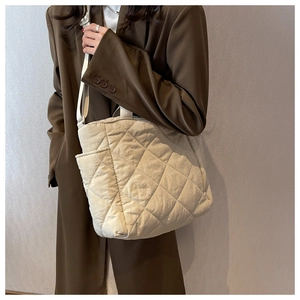 Close-up of quilted beige tote bag showing oversized diamond stitching and side pocket details