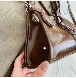 Close-up of brown glossy leather handbag showing triangular structure and silver buckle