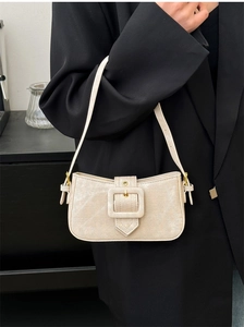Detail of cream shoulder bag with twill texture and gold buckle on a black suit