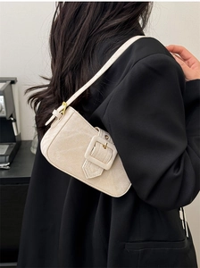 Detail of beige shoulder bag with oversized buckle shown on model in black suit