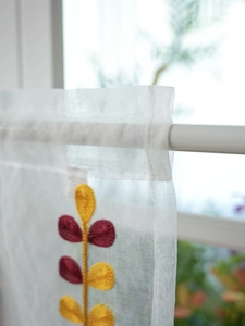 Detail of white sheer café curtain with yellow and red leaf embroidery on rod