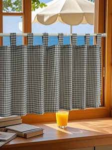 Detail of black and white gingham tab top cafe curtain in a sunny window setting