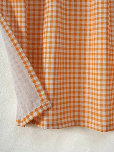Detailed close-up of orange and white gingham cotton linen fabric with refined stitching