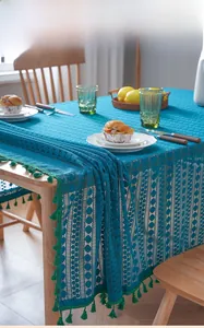 Detail of dark teal lace tablecloth with vibrant green tassels on a wooden dining table