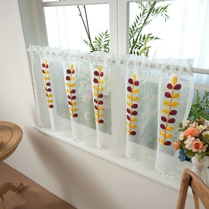 White semi-sheer cafe curtain with yellow leaf embroidery and pom-pom trim on window