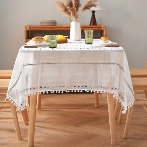 Minimalist white rectangle tablecloth with pom-pom tassels on a wooden dining table