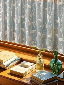 Dettaglio della tenda in pizzo beige con motivi di uccelli e bordo ondulato