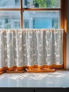 Dettaglio della tenda in pizzo beige con motivo di uccelli e bordo ondulato