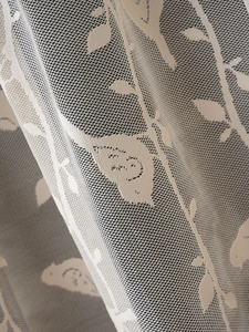 Primo piano della tenda in pizzo beige con ricami dettagliati di uccelli e fiori