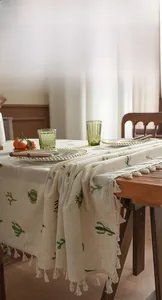Detailed view of white linen tablecloth with green cactus embroidery and tassel fringe edges