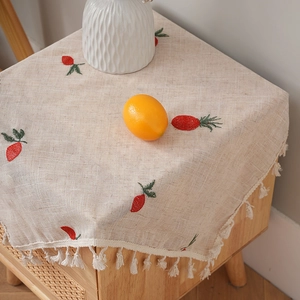 Tovaglia in lino con nappe e ricami di frutta su un comodino in legno di pino