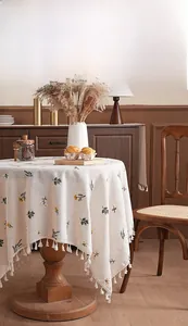 Detail of embroidered beige linen tablecloth with floral patterns and fringed tassel edges