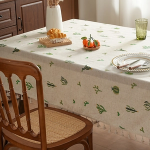 Thick linen tablecloth with green cactus embroidery and white tassel trim on wood table