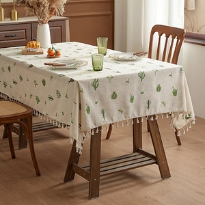 Pastel linen tablecloth with green cactus prints and white fringe trim on a wooden table