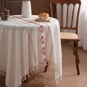 White cotton tablecloth with red geometric embroidery and tassels in a cozy home setting