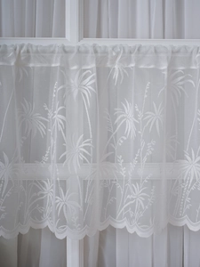 Detail of white lace cafe curtain with tropical palm leaf pattern and scalloped hem