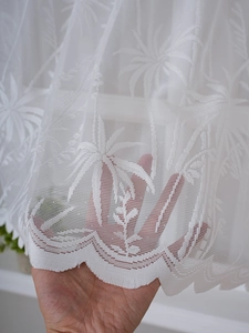 Detail of white lace cafe curtain with embroidered palm leaf patterns and mesh texture