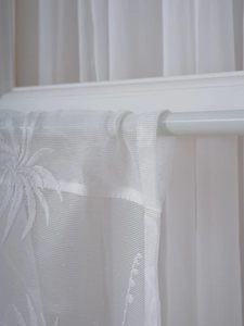Close-up of white lace curtain showing delicate tropical leaf embroidery and rod pocket detail