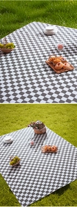 Detail of waterproof black and white checkered picnic mat spread on green grass