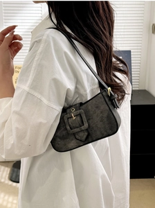 Detail of black denim underarm bag with wide buckle strap and gold hardware
