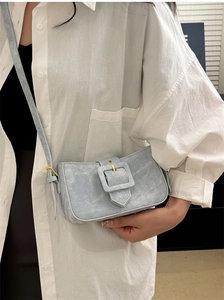 Detail of light blue denim baguette bag featuring a large gold buckle and adjustable strap