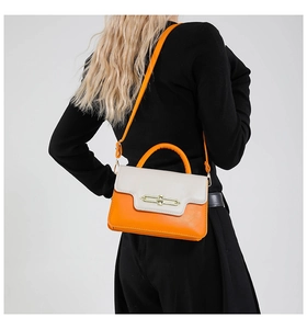 Detail of a chic orange and beige crossbody bag with a gold metal ring lock on a model