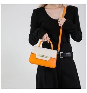 Detail of a bright orange crossbody bag with cream flap and gold rectangular lock