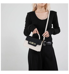 Detail of a two-tone contrast flap handbag with gold metal clasp on a gray background