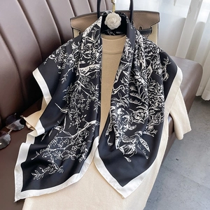 Fashionable black and white floral silk square scarf elegantly draped over a sweater