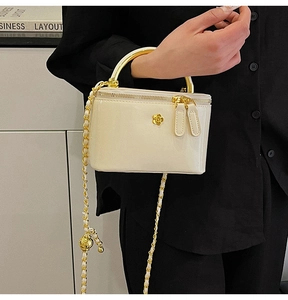Detail of cream glossy mini bag featuring gold tube handle and camellia emblem