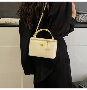 Close-up of cream glossy bag with gold metal handle and chain strap on a model