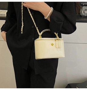 Close-up of cream glossy leather handbag with gold floral logo and metal handle