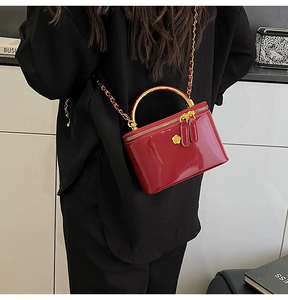 Detailed view of a red glossy patent leather mini bag with gold chain and flower charm