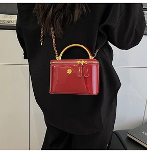 Detail of red patent leather vanity case bag with gold metal handle and camellia floral decor