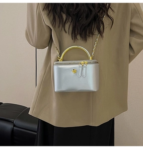 Detail of silver chain bag featuring a gold floral logo and metallic top handle