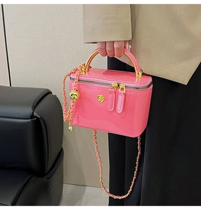 Close-up of pink patent leather crossbody bag with gold metal handle and woven chain strap