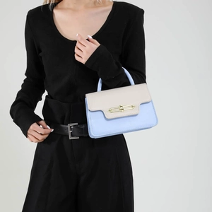 Chic light blue and cream contrast handbag with gold chain buckle held by a model