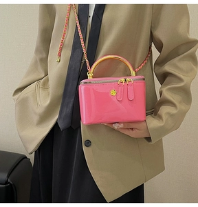 Detail of a pink glossy leather handbag with gold handle on a model in a khaki suit